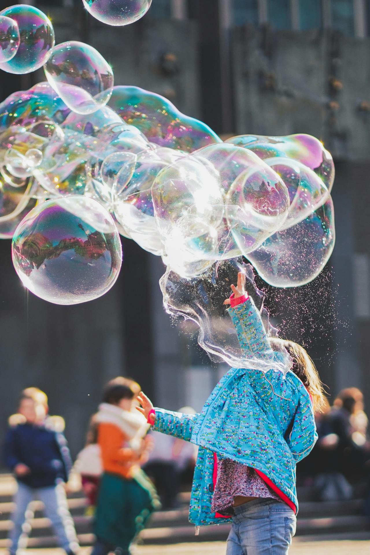 A girl enjoying playing with some big bubbles above her head.