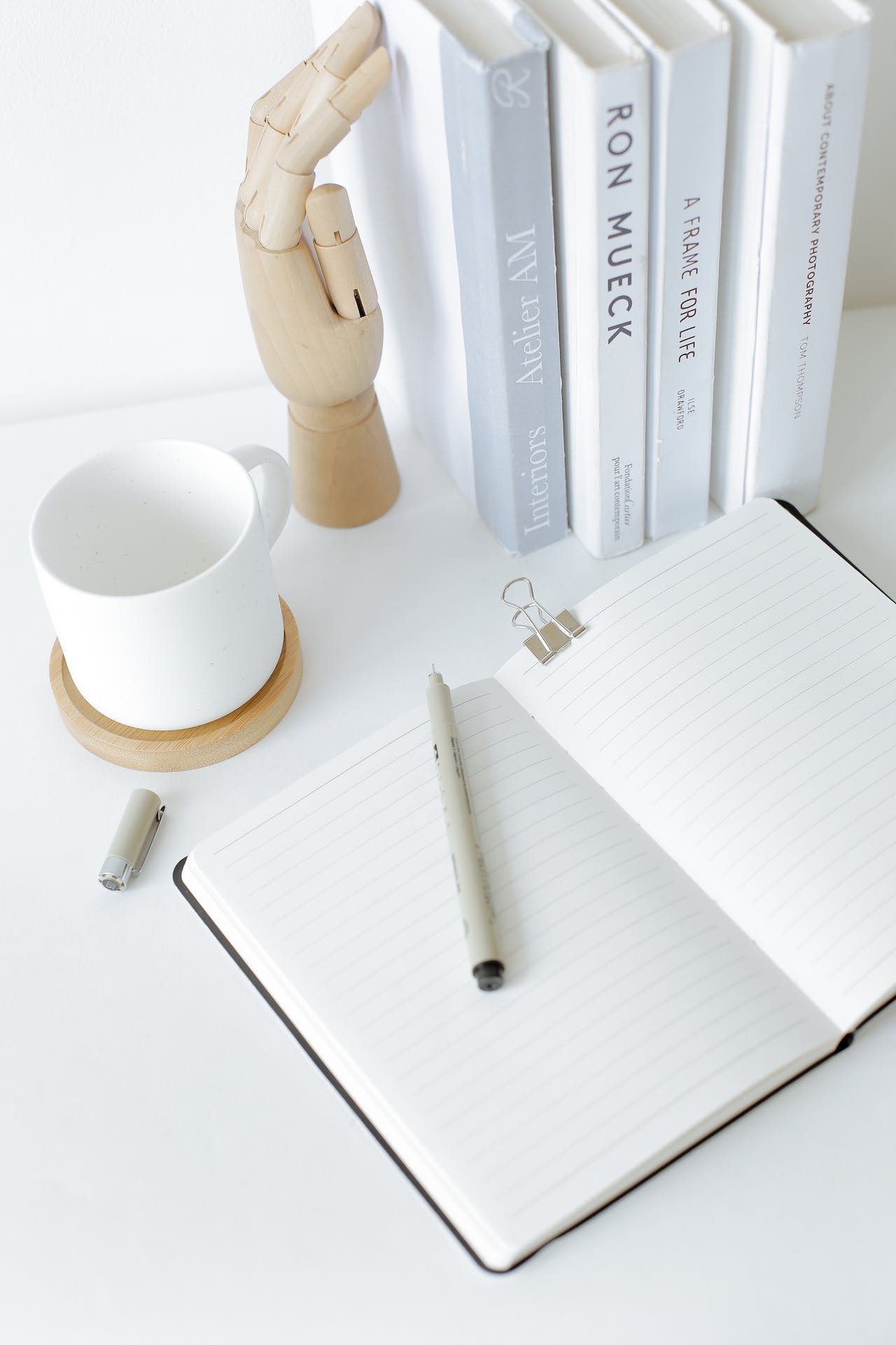 A notebook put on a desk with a pen on it and a coffee cup and some books next to it.