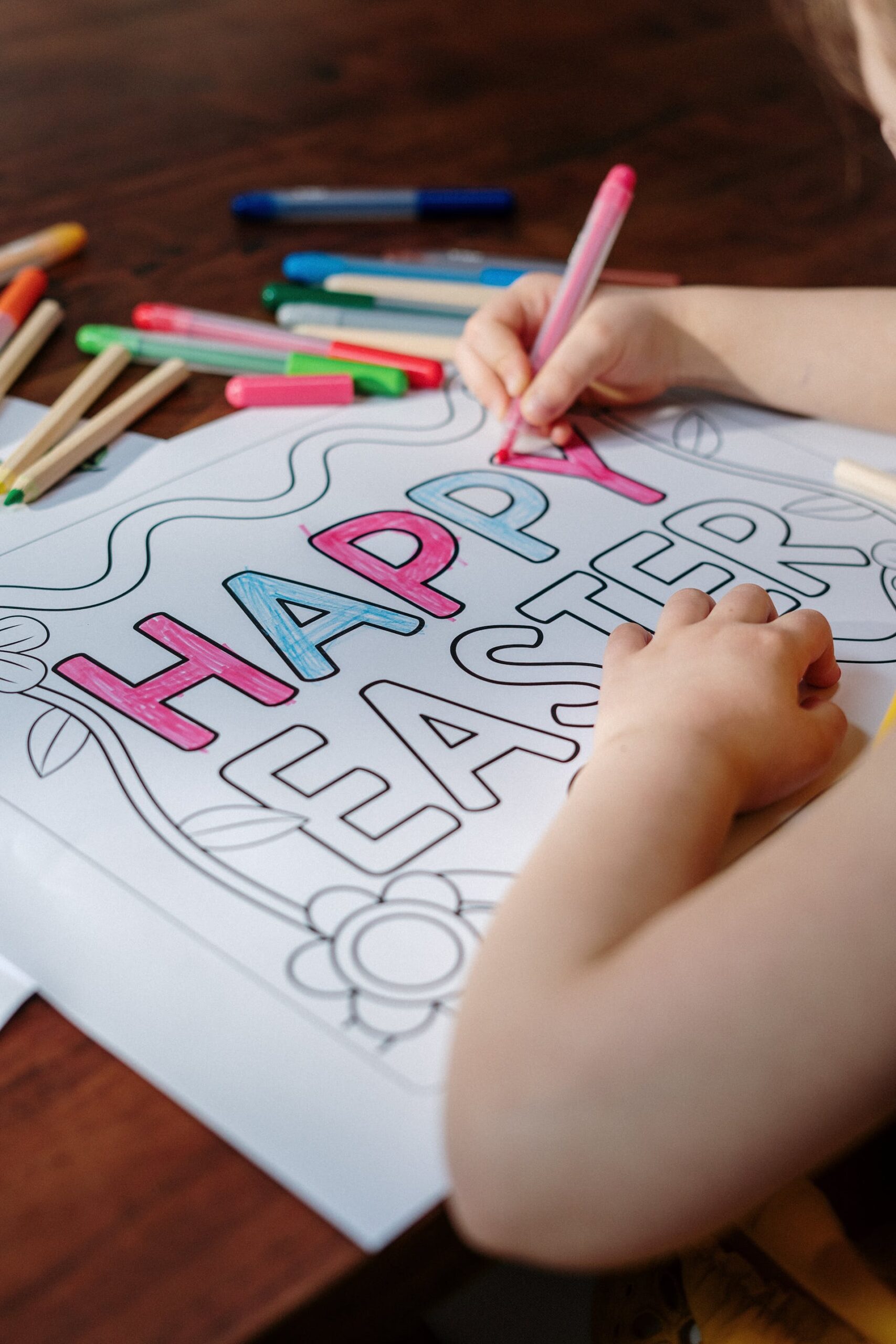 A person, who seems to be a little child, holding a coloring pencil and coloring on the words "Happy Easter".