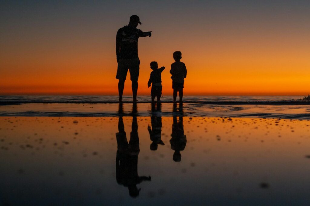 A father with two children on a beach during sunset.