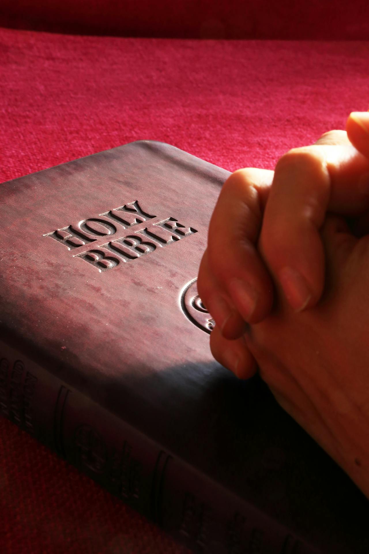 Hands holding each other for prayer with a Bible next to them.